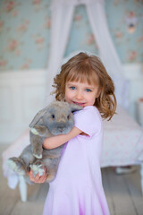 A pretty little girl stands and holds a large Easter bunny in her hands.