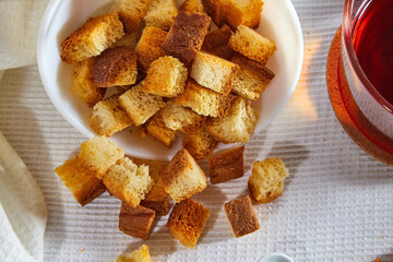 Square toasted pieces of homemade delicious rusk, hardtack, Dryasdust, zwieback on a plate and black tee in a cap on a white tablecloth.