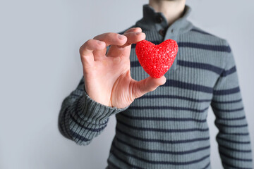 young guy in jacket holding a red heart model in his hand, a symbol of love, concept of confession,...