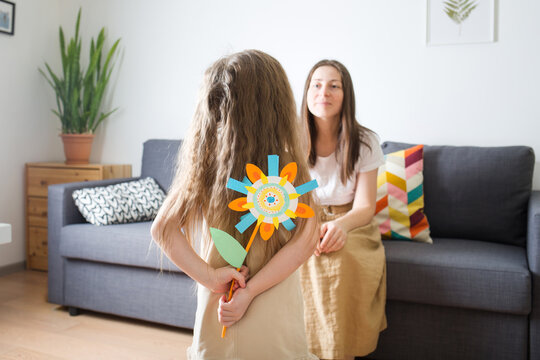 mother's day. child gives her mom flower made of paper. baby girl. girl hides craft in her hands. diy create art for kids.