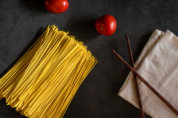 Yellow spaghetti and tomatoes on a black marble table. Yellow Italian Pasta. Raw spaghetti. Italian concept and menu