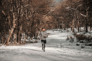 Fototapeta na wymiar Runner running in forest at snowy winter day. Winter fitness, sporty lifestyle, healthy life