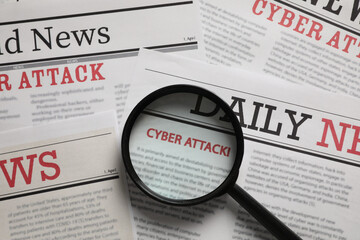 Newspaper with headline CYBER ATTACK under magnifying glass, top view