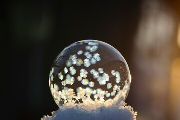 A frozen bubble in the snow with bokeh in the background. Beautiful frosty patterns on a frozen soap bubble. winter, frosty background. Frozen bubble at sunset light. soap bubble on snow close up