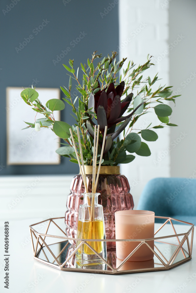 Wall mural Beautiful bouquet with eucalyptus branches, candle and aromatic reed air freshener on white table indoors. Interior elements