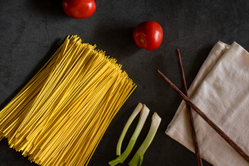 Yellow spaghetti and tomatoes on a black marble table. Yellow Italian Pasta. Raw spaghetti. Italian concept and menu