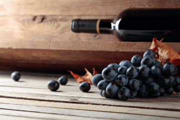 Bottle of red wine and a bunch of grapes on an old wooden table in the wine cellar.