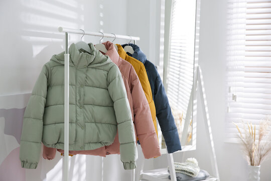 Different warm jackets hanging on rack indoors