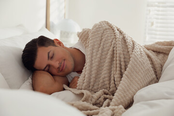 Man covered with warm beige plaid lying in bed indoors