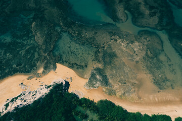 Top down aerial view of seashore and coral reefs close to tropical forest vegetation at Praia do Espelho, Bahia, Brazil. Nice green sea and golden brown sand. Post pandemic travel destination.