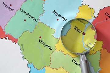 Metal magnifying glass above Kyiv region on map of Ukraine, closeup