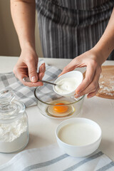 The process of preparing the dough at home. The woman adds the cream cheese to the bowl with the eggs. Vertical photo. Homemade food.