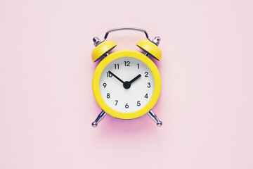 Yellow vintage alarm clock on a pink background. Daylight saving concept. Flat lay, copy space.