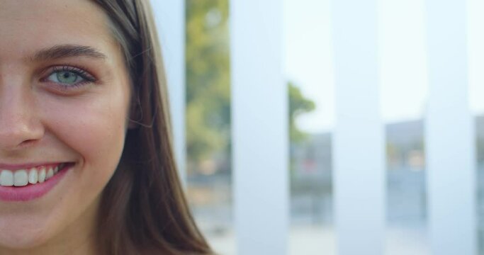 Portrait of joyful beautiful female with long hair and green eyes smiling at street. Close up of half face of pretty woman with happy smile outdoor at bus stop. Train station. Travel, tourism concept