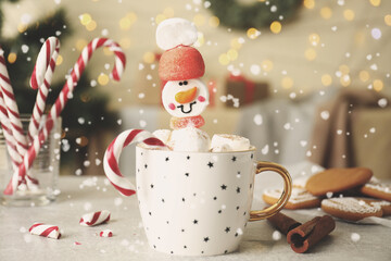 Funny marshmallow snowman in cup of hot drink on light grey table