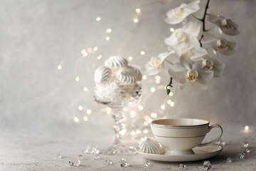 Cozy home spring breakfast still life. A porcelain cup of hot green tea with a marshmallow dessert on a gray background is decorated with a flowering branch of a white otchid. Spring concept. 