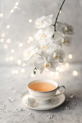 Cozy home spring breakfast still life. A porcelain cup of hot green tea with a marshmallow dessert on a gray background is decorated with a flowering branch of a white otchid. Spring concept. 