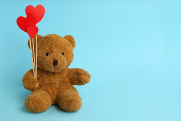Cute teddy bear with red hearts on light blue background, space for text. Valentine's day...