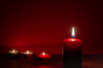 Burning red candle at night and other candles on dark background