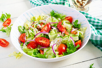 Fresh tomatoes with cucumber, lettuce, red onion and spices in a white bowl.  Concept healthy appetizer. White wooden background.