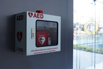 Heart defibrillator in white box on the wall with Thai word mean "Automated External Defibrillator". Automated External Defibrillator (AED) on the wall.