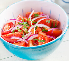Fresh tomatoes with red onion and spices in a blue bowl.  Concept healthy appetizer. White wooden background.