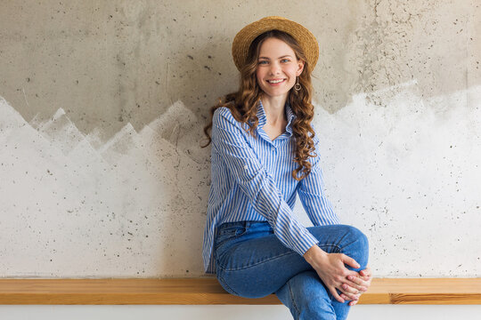young attractive stylish woman sitting at wall background, straw hat