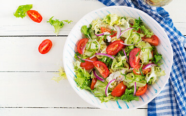 Fresh tomatoes with cucumber, lettuce, red onion and spices in a white bowl.  Concept healthy appetizer. White wooden background. Top view, overhead, copy space