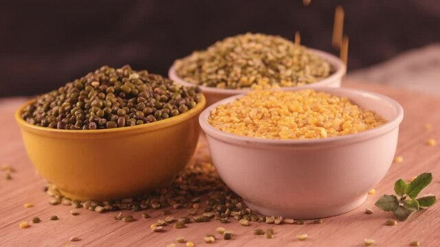 Falling Yellow moong dal, Indian pulse, yellow mong dal and green Moong bean with green mung daal on wooden table, healthy lentil pulse bean on table,falling moong dal on white bowl