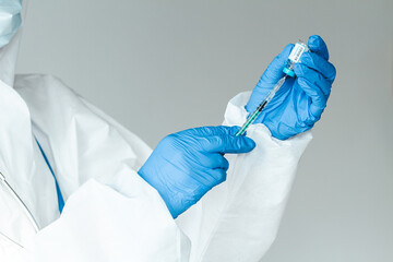 Doctor or nurse in a protective suit holds a syringe and covid 19 vaccine