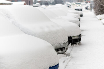 Snow covered cars parked in a row next to each other. Cars on street in cold winter.