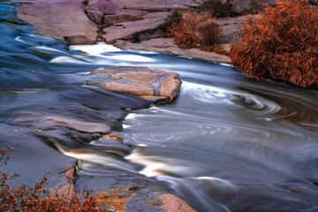 Stream runs among white wet stones covered with grass in golden autumn