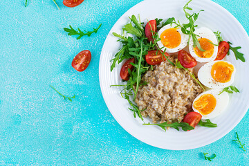 Breakfast oatmeal porridge with boiled egg, cherry tomatoes and arugula. Healthy balanced food. Top view, above, copy space