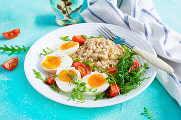 Breakfast oatmeal porridge with boiled egg, cherry tomatoes and arugula. Healthy balanced food.