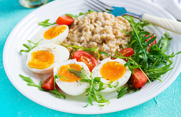 Breakfast oatmeal porridge with boiled egg, cherry tomatoes and arugula. Healthy balanced food.