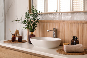 Vase with beautiful branches, candles and air reed freshener near vessel sink in bathroom. Interior design