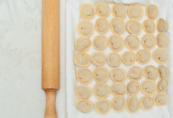 Raw dumplings or pelmeni with minced meat filling and rolling pin. The process of making dumplings. Cooking at home concept. Tradition home-made food.