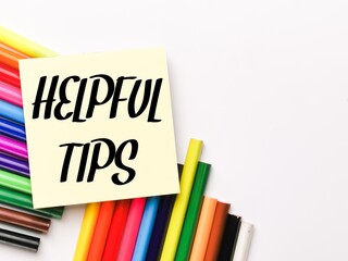 Text HELPFUL TIPS on paper note with colorful pencils isolated on white background.