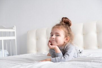 little girl in grey turtleneck having fun on white bedding