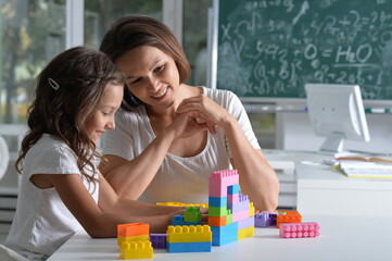  little daughter and mother playing with colorful plastic blocks at home