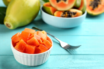 Dices of fresh ripe papaya in bowl on turquoise wooden table