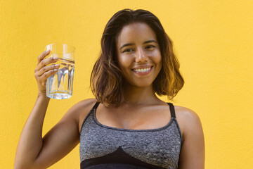 Healthy, smiling young woman with a glass of water on a yellow background