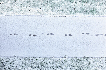 Single line of footsteps in fresh snow in the middle of sidewalk, grass on both sides, top view