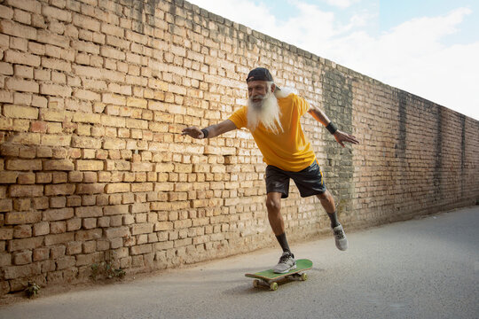 A BEARDED OLD MAN ENTHUSIASTICALLY USING SKATE BOARD	