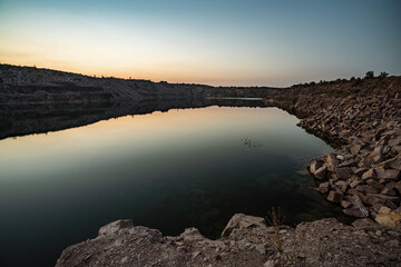 Old flooded stone quarry surrounded by stone waste from a mine work against a beautiful night sky