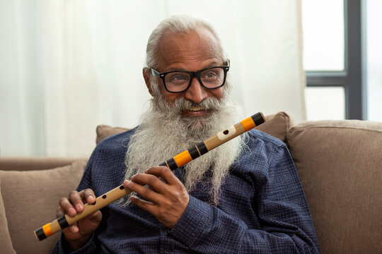 A BEARDED OLD MAN SMILING WHILE PLAYING FLUTE	