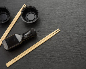 wooden sticks for sushi, bottle of soy sauce and disposable plastic plates on black background