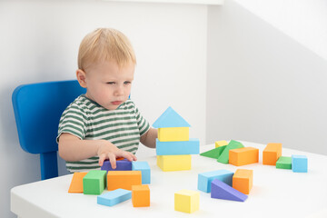 Little boy playing with colorful blocks at table on white background.
