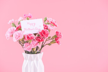 Mother's Day holiday gift design concept, pink carnation flower bouquet with greeting card, isolated on light pink background, copy space.