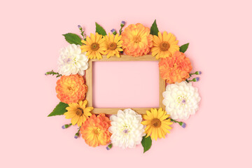 Top view of flower border frame made of dahlia, arnica and green leaves on a pink background. Greeting card template with copyspace.